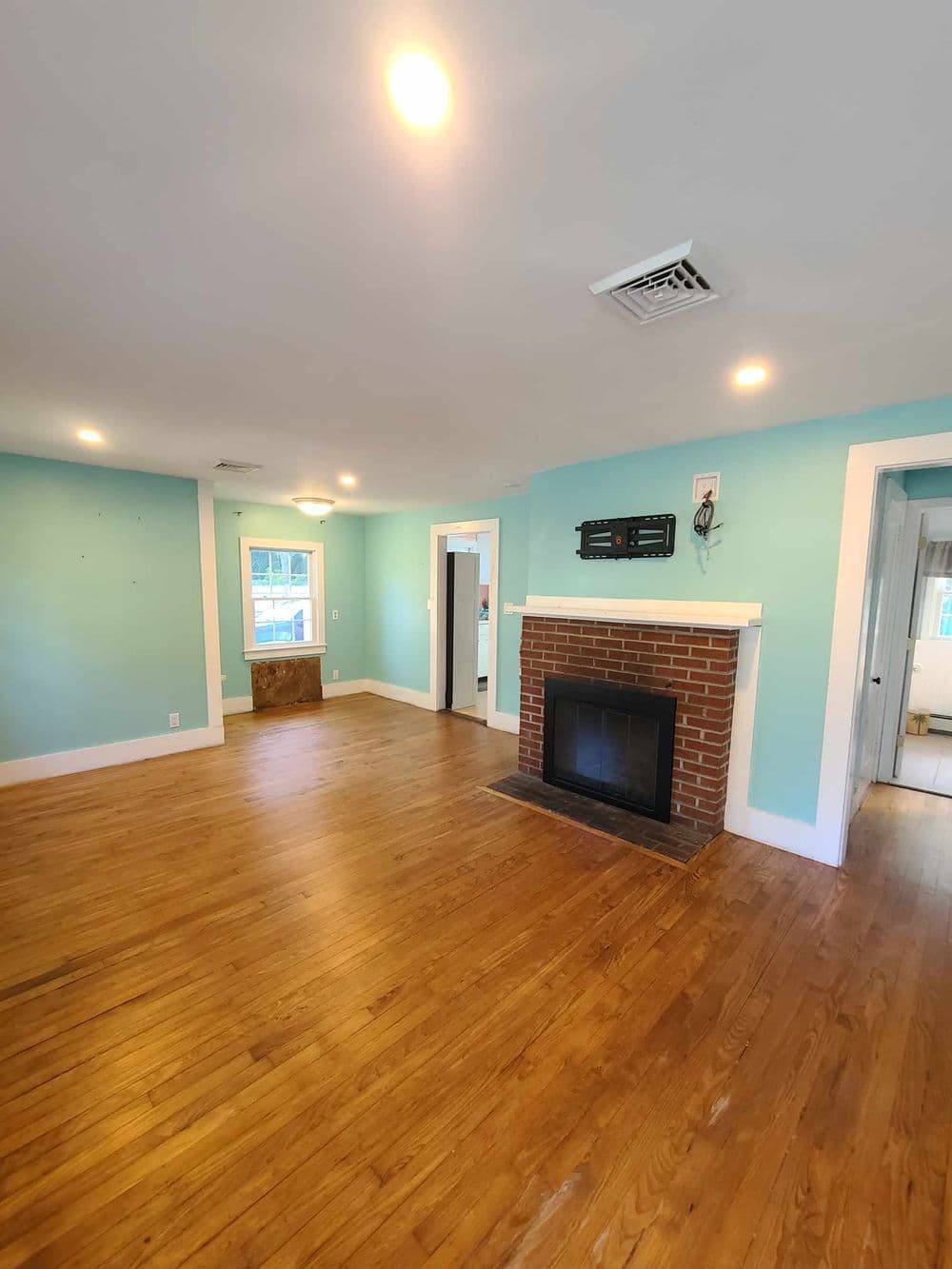 Spacious living room with teal walls, hardwood floors, and a brick fireplace.