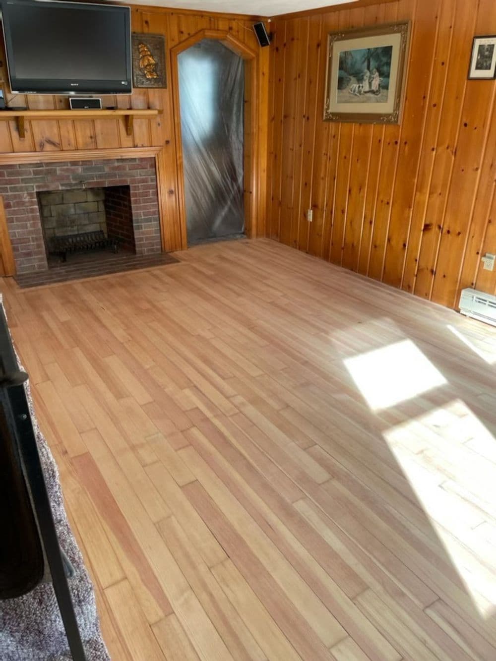 Living room with wooden flooring, brick fireplace, and natural light from window.