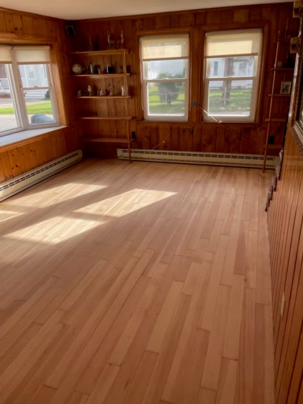 Bright, spacious wood-paneled living room with large windows and polished hardwood flooring.