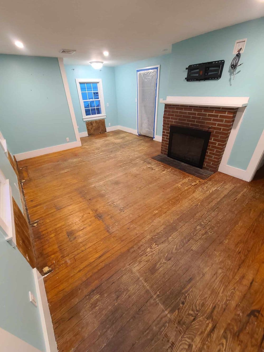 Living room with blue walls, wooden floors, fireplace, and renovation work in progress.