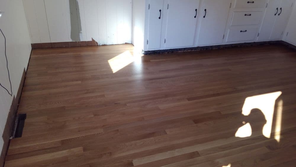 Newly installed hardwood flooring in a bright kitchen with white cabinets.