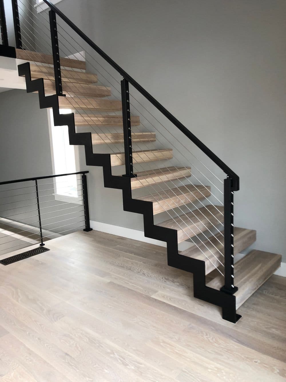 Modern wooden staircase with sleek black railing and cable details in a minimalist interior.