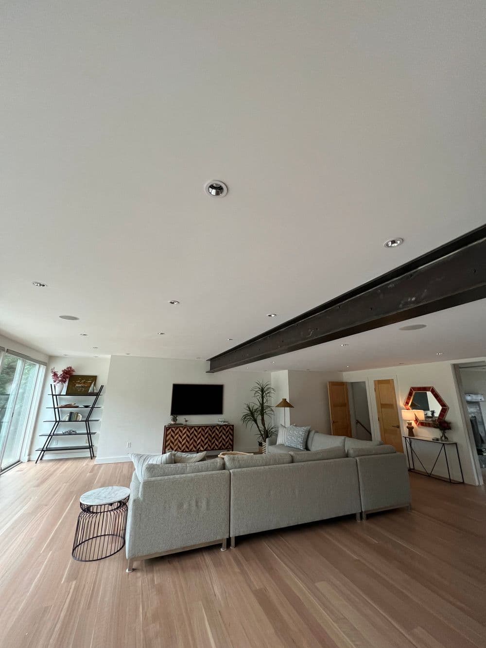 Modern living room with a light gray sectional sofa, hardwood floors, and large windows.