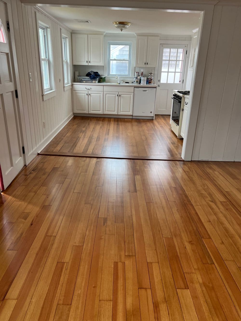 Spacious kitchen with hardwood floors and white cabinetry, natural light streaming in.