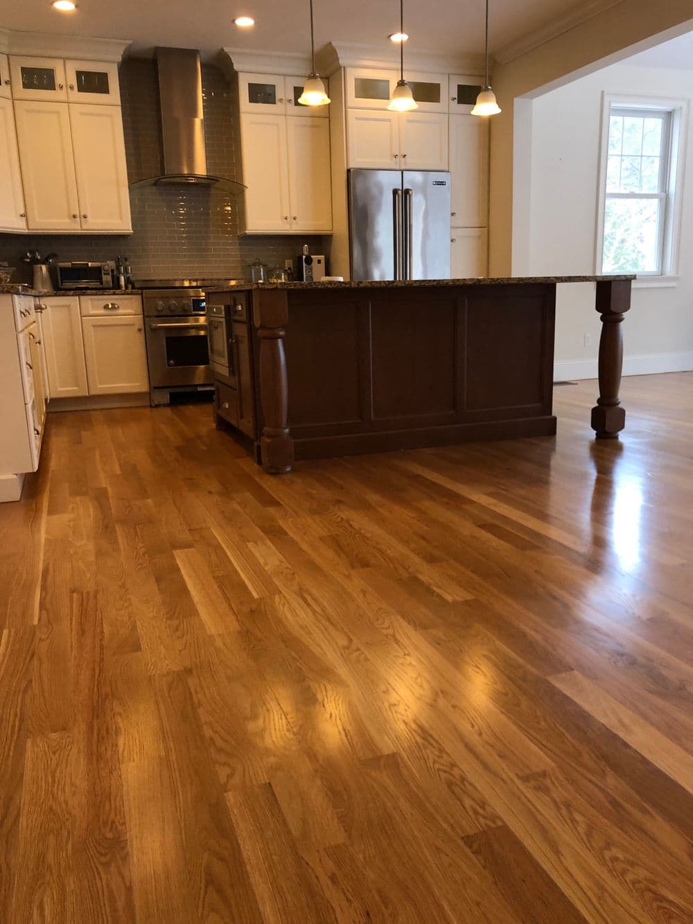 Modern kitchen with hardwood floors, sleek island, stainless steel appliances, and bright lighting.