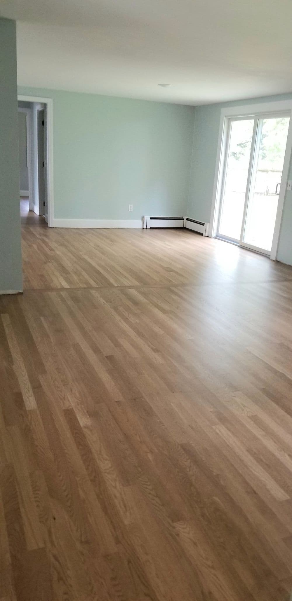 Spacious living room with light-colored hardwood floors and sliding glass doors to outdoor area.