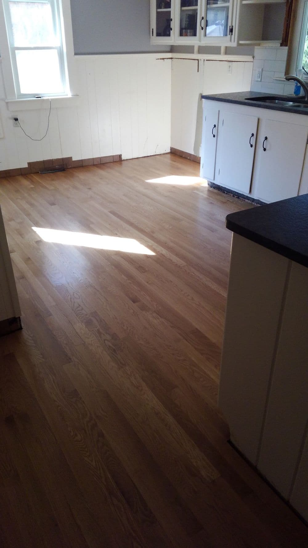 Sunny kitchen with light-colored hardwood flooring and white cabinets.