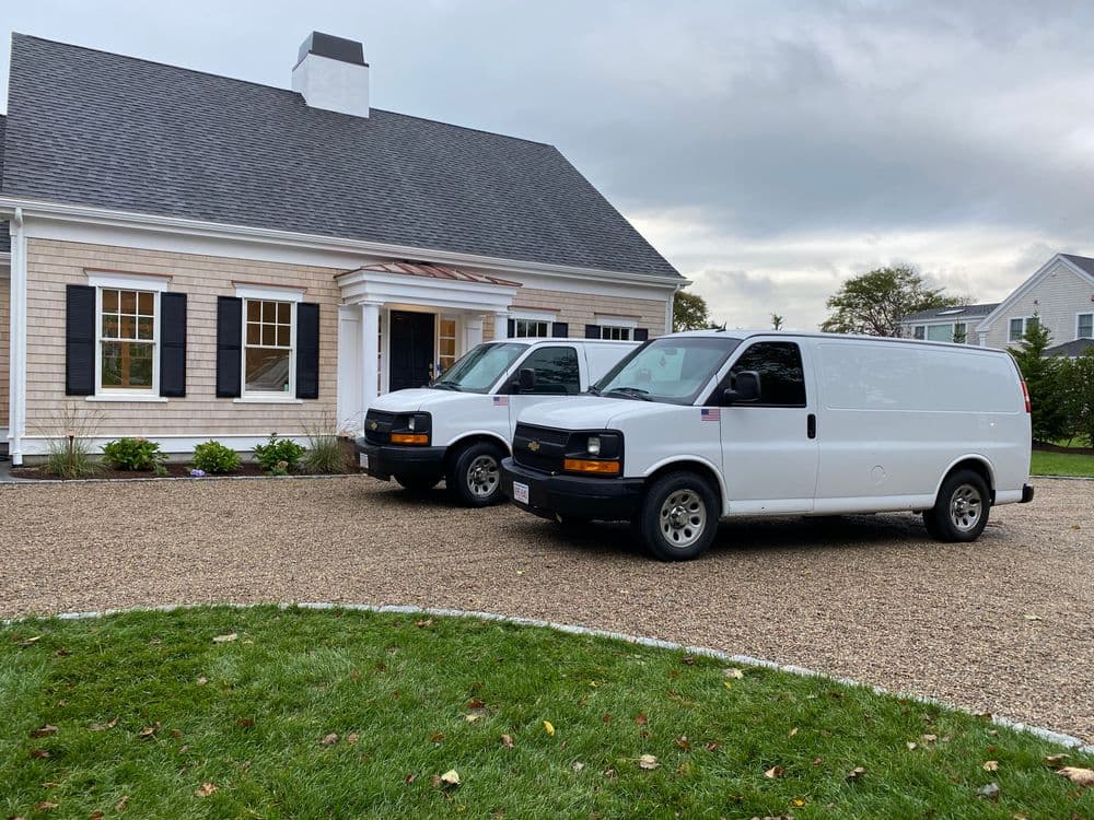 Two white service vans parked in front of a modern house with a gravel driveway.