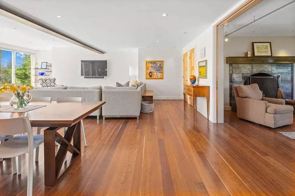 Modern living room and dining area with wooden floors, large windows, and stylish furniture.