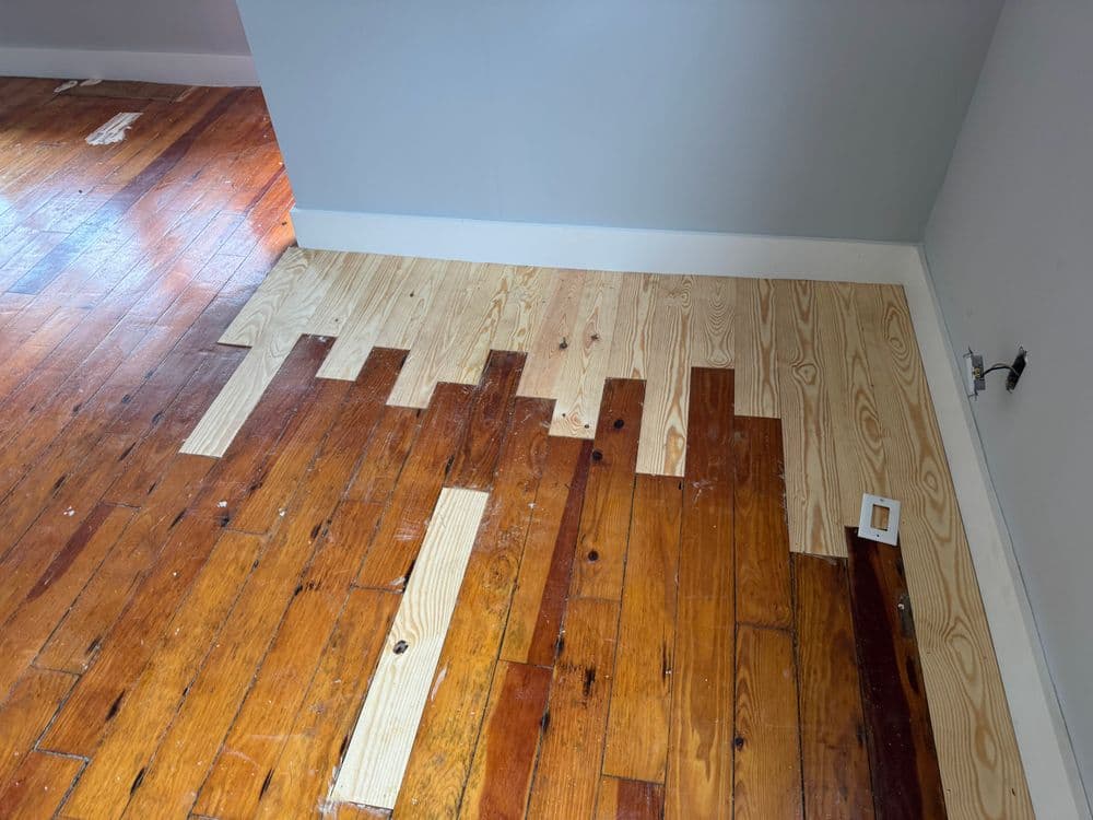 Wood floor renovation with contrasting new and old hardwood planks in a partially finished room.