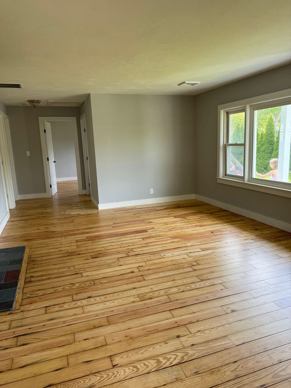 Spacious living room with hardwood floors and large windows, bright natural light.